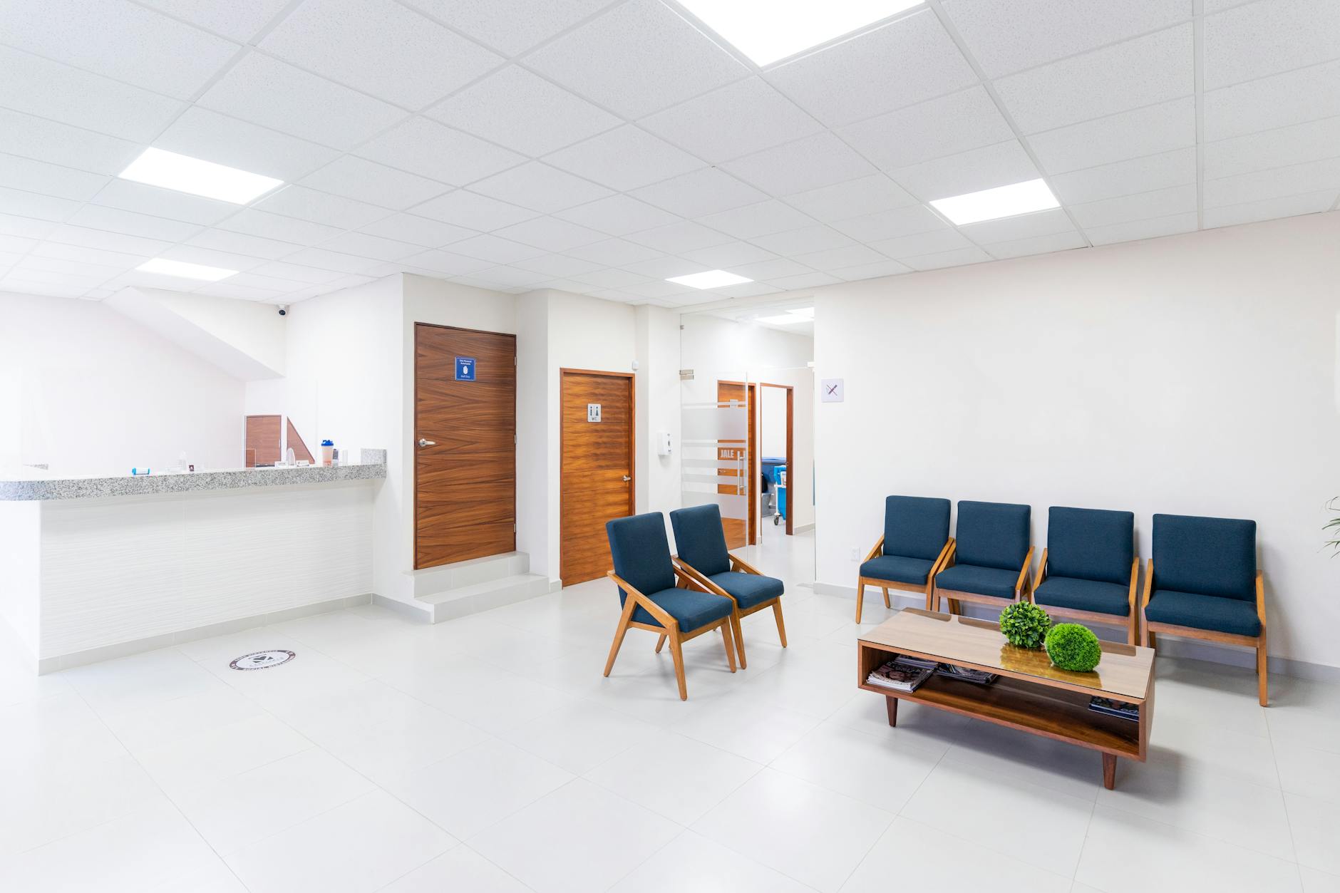 Warm welcoming interior of a medical clinic waiting room, comfortable seating, teal and neutral decor, potted plant, clean professional suburban medical office, soft warm lighting, inviting and calm atmosphere, photorealistic interior photography